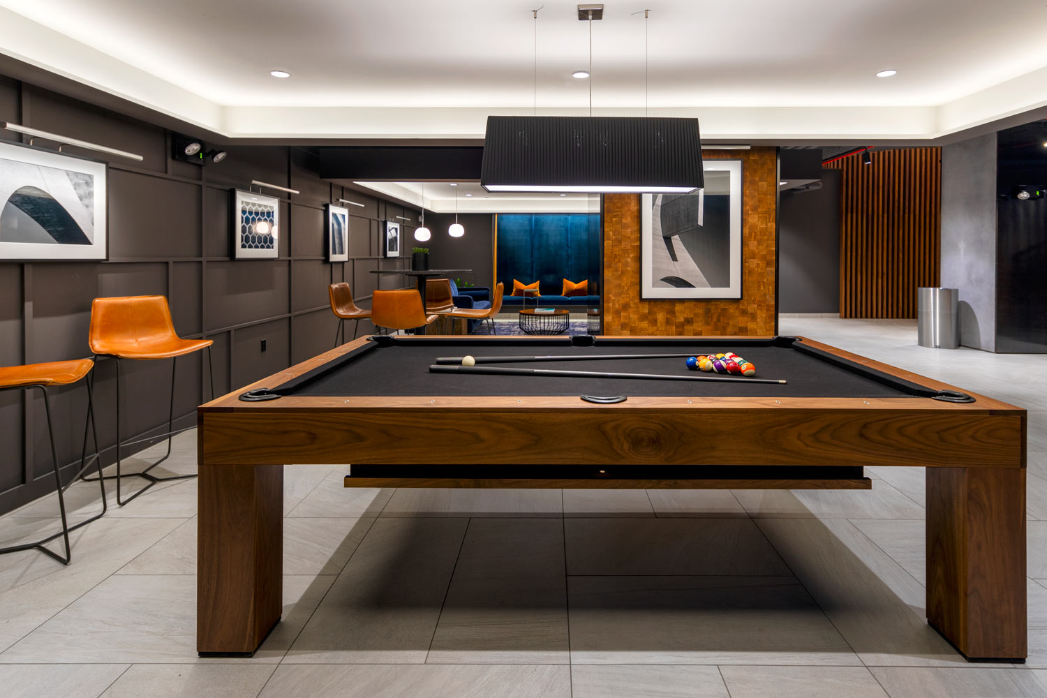 Black felt top pool table in modern lounge with dark walls and high leather chairs and marble floors