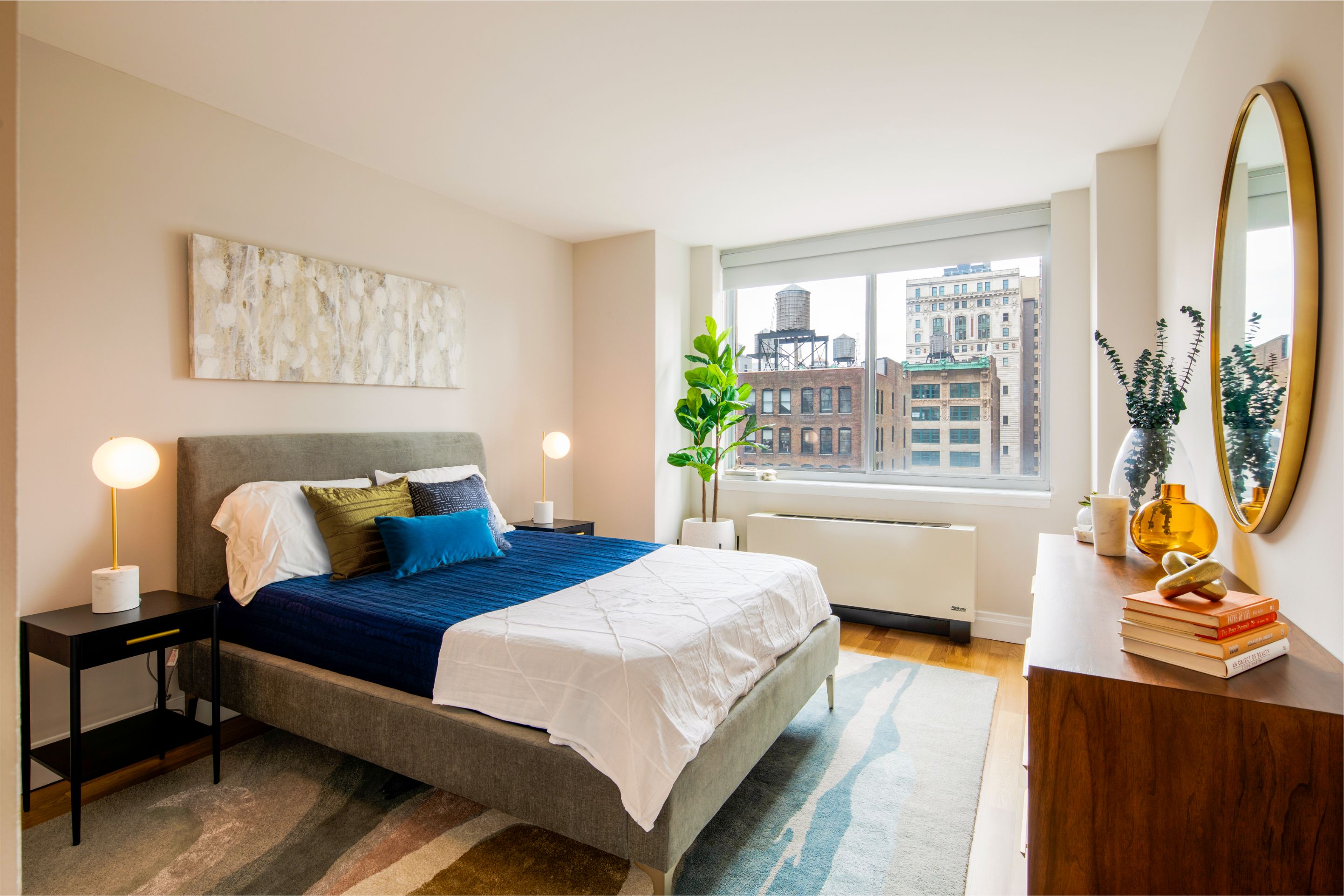 bedroom with bed, two side tables and dresser with fiddle leaf fig and skyscrapers through a window